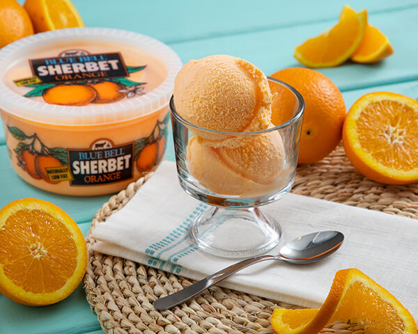 Blue Bell Orange Sherbet in small glass with sliced oranges.